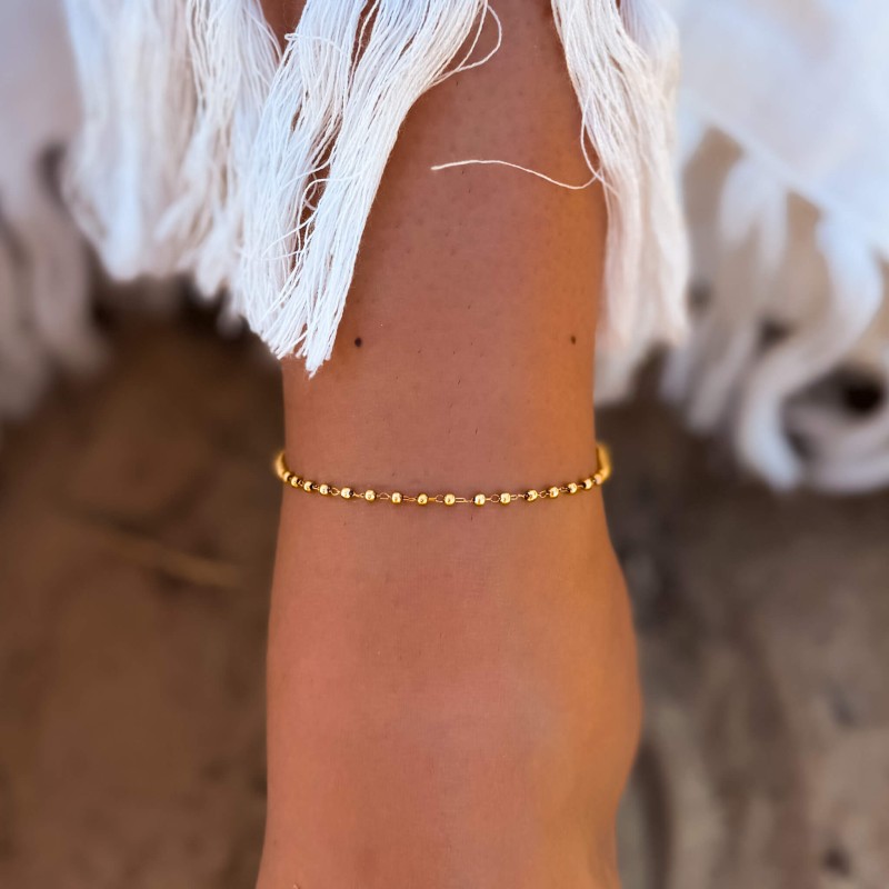Złota bransoletka na kostkę z kuleczkami ze stali nierdzewnej na nodze modelki. Minimalistyczna biżuteria letnia, idealna do stylizacji na lato, wakacje, plażę i codzienne noszenie
