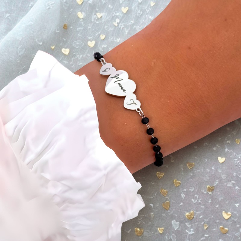 Bransoletka personalizowana wykonana ze srebrnej stali chirurgicznej, ozdobiona czarnymi koralikami. Na nadgarstku prezentuje się elegancko, z sercem Mama w centrum i mniejszymi serduszkami po bokach z grawerem inicjałów dzieci.