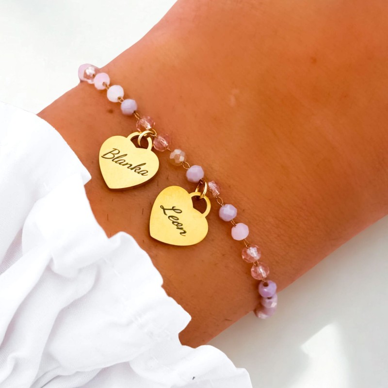 Bransoletka dla mamy z 2 serduszkami i grawerem imion dzieci – różowe koraliki i pozłacane zawieszki pokazane na nadgarstku kobiety, elegancka biżuteria personalizowana
