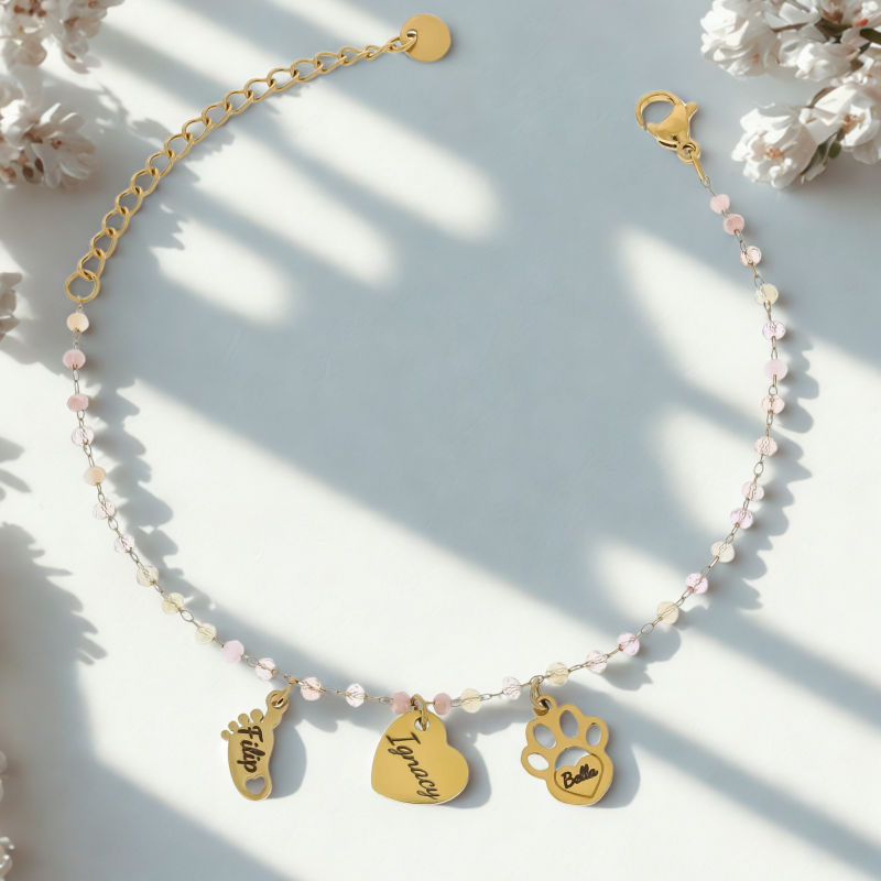 Pozłacana bransoletka personalizowana z grawerem imion, ozdobiona pastelowymi koralikami i zawieszkami w kształcie serca, dziecięcej stópki oraz psiej łapki. Biżuteria ze stali chirurgicznej, idealna jako prezent dla mamy, babci lub właściciela pupila.