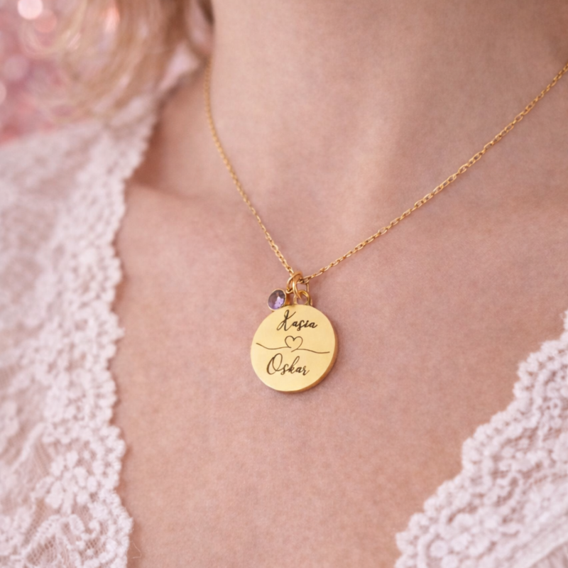 Personalizowany złoty naszyjnik z okrągłą zawieszką i grawerem z imionami nadaje biżuterii romantycznego charakteru. Idealny prezent na rocznicę lub wyjątkową okazję.