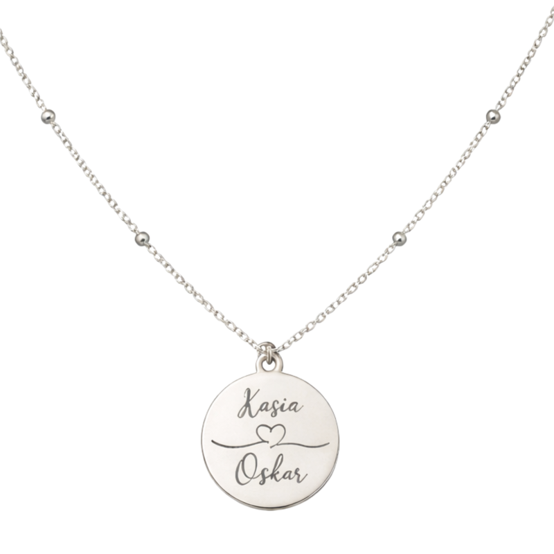 Personalizowany srebrny naszyjnik z okrągłą zawieszką 2 cm, ułożony w kształt litery V na białym tle. Delikatny łańcuszek i precyzyjny grawer imion podkreślają elegancki, minimalistyczny charakter biżuterii.